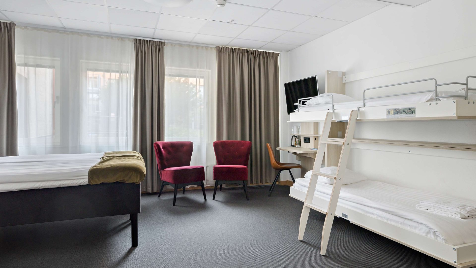 Ett hotellrum med en dubbelsäng, två fåtöljer och en våningssäng.