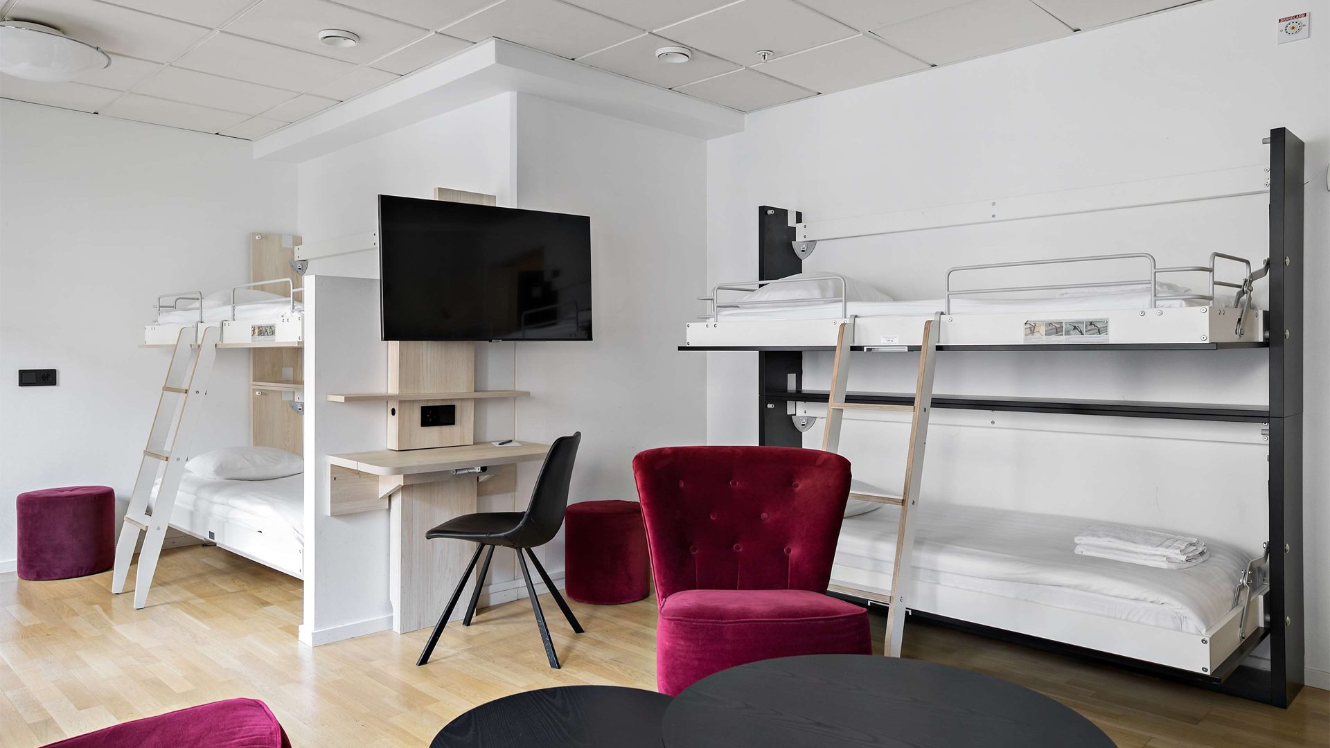 Ett stort hotellrum med två våningssängar, ett skrivbord och en tv.